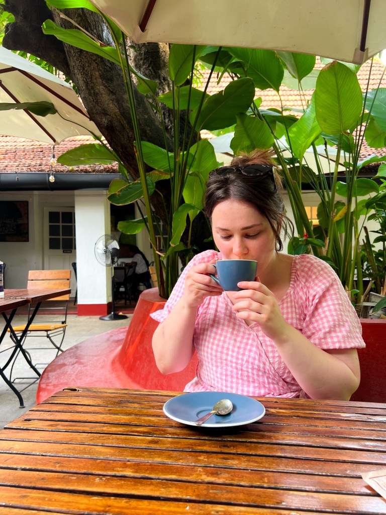 Drinking coffee wearing pink gingham dress in the restaurant Pandhal in Fort Kochi, South India